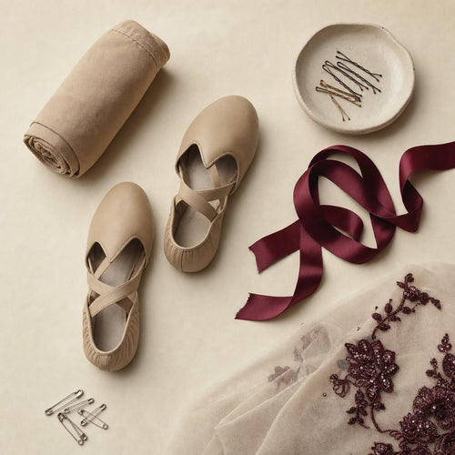 Dance shoes, tights, hair pins and a burgundy ribbon arranged on cream paper
