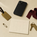 A brass luggage tag, phone, blank planner card and burgundy ribbon on cream